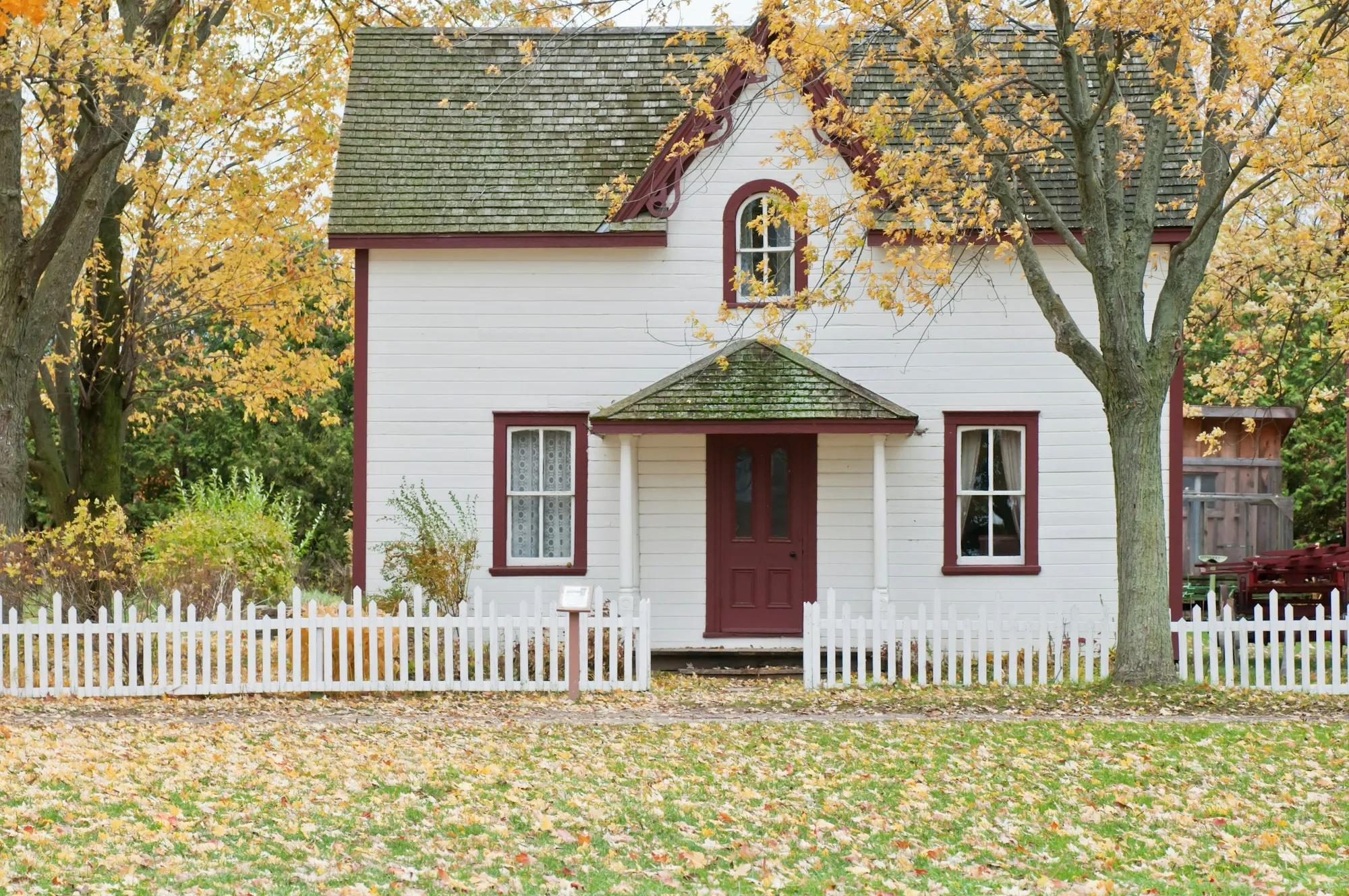 White house with a red door behind a white picket fence