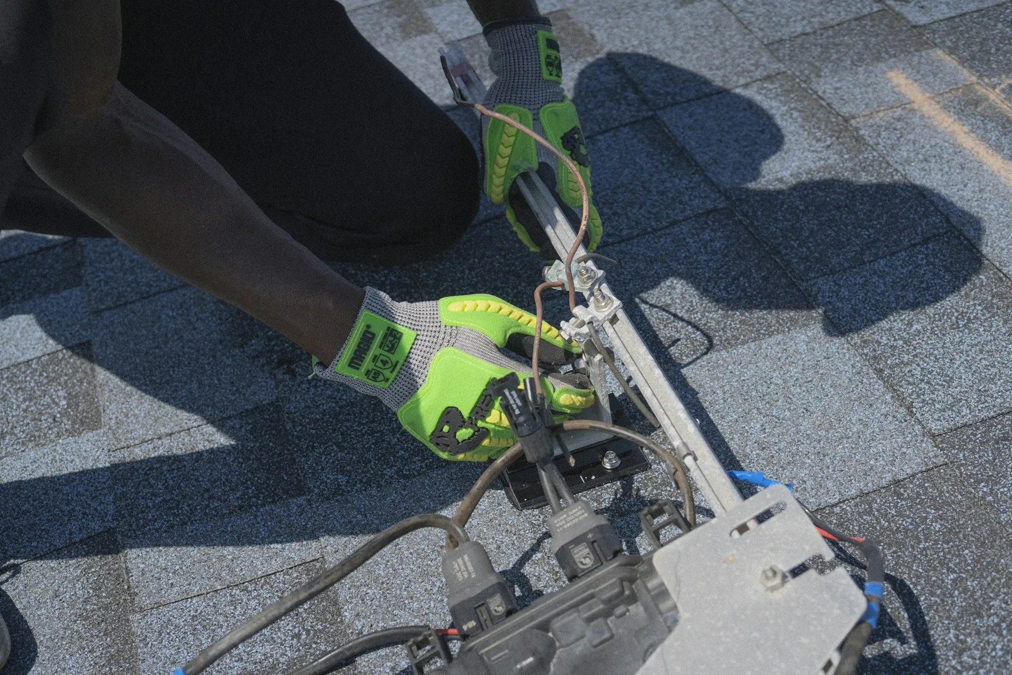 Gloved hands fastening a solar rail mount to a shingle roof